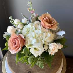 Low arrangement of white hydrangeas with peach roses and white accent blooms in a rounded design