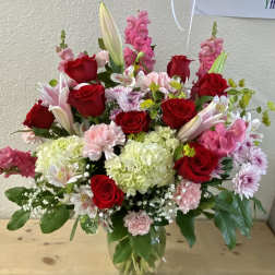 Mixed bouquet of red roses, pink flowers, and white lilies in a glass vase