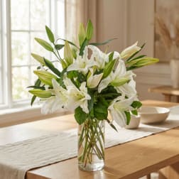 White lilies in a clear glass vase on a dining table