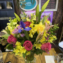 Mixed bouquet of pink roses, yellow daffodils, and purple iris in a glass vase