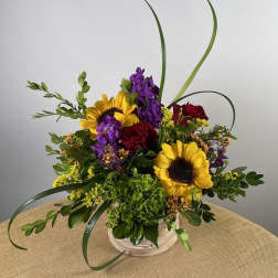 Bouquet of sunflowers, red roses, and purple flowers in a white basket