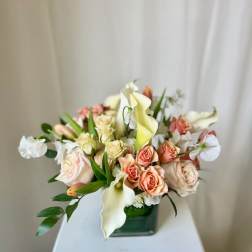 Arrangement of peach roses and white calla lilies in a square glass vase