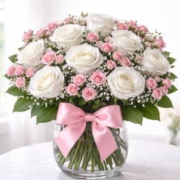 White and pink rose bouquet in a glass vase with a pink ribbon