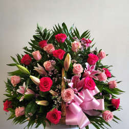 Basket arrangement of pink and red roses with lilies and a pink ribbon