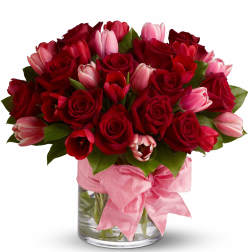 Red roses and pink tulips in a glass vase with a pink ribbon