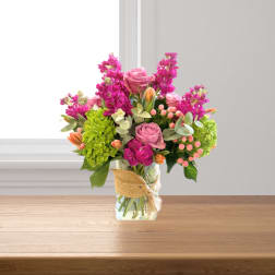Pink roses and magenta flowers in a glass vase with burlap ribbon