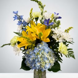 Bouquet of yellow lilies, blue hydrangea, and white daisies in a glass vase