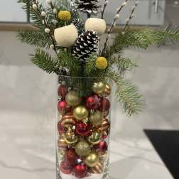 Holiday arrangement in a glass vase with pinecones and red-gold ornaments