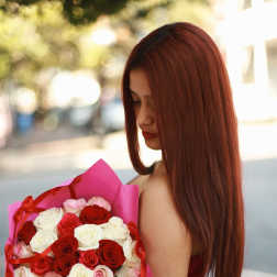 Woman holding a bouquet of red, white, and pink roses wrapped in pink paper