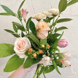 Handheld bouquet of pale pink roses and alstroemeria with greenery