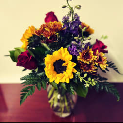 Bouquet of sunflowers, purple flowers, and red roses in a glass vase