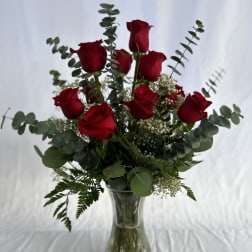 Tall arrangement of red roses with eucalyptus and white filler flowers in a clear glass vase