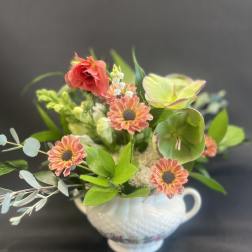 Mixed floral arrangement in a white handled vase with coral and green blooms