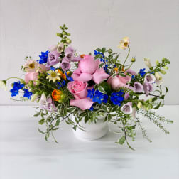 Pink and blue mixed flower arrangement in a white vase