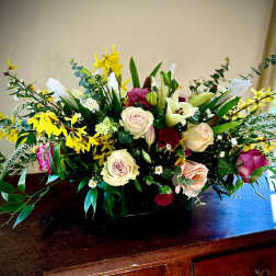 Low centerpiece of ivory roses, white lilies, yellow blooms and pink flowers in a black rectangular vase