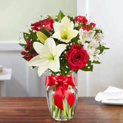 Bouquet of red roses and white lilies in a glass vase with a red ribbon