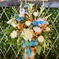 Tall bouquet of white and blue flowers in a glass vase with ribbon