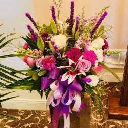 Tall bouquet of pink, white, and purple flowers in a dark vase with ribbon