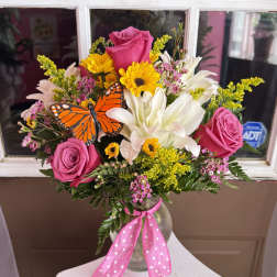 Pink roses and white lilies in a glass vase with a butterfly accent