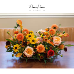 Low floral centerpiece with orange, yellow, and peach blooms in a shallow container