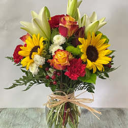 Mixed bouquet of sunflowers, roses, lilies, and carnations in a glass vase