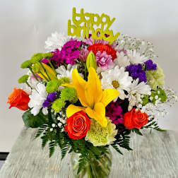 Colorful birthday bouquet in a glass vase with a yellow topper