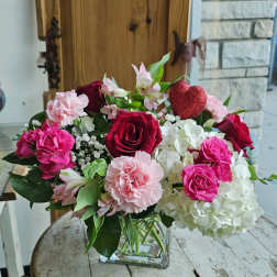 Mixed pink and white flowers in a clear glass vase with a red heart pick