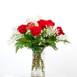 Red roses and small white flowers arranged in a clear glass vase