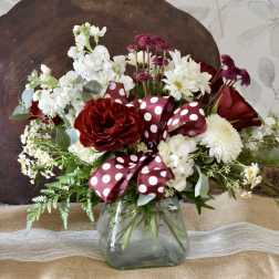 Red and white flower arrangement in a glass vase with a polka-dot ribbon