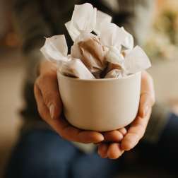 Hands holding a white bowl filled with wrapped chocolates