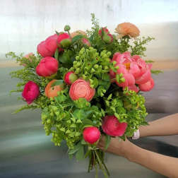 Handheld bouquet of pink and peach flowers with lush greenery