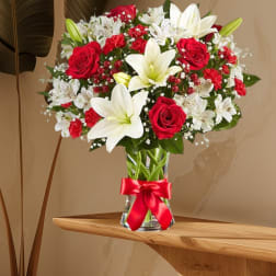 Red roses and white lilies arranged in a clear glass vase with a red ribbon