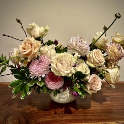 Low arrangement of cream roses, pink mums, and ranunculus in a white ceramic bowl