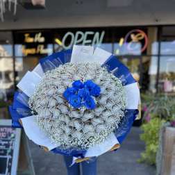 Bouquet of blue roses surrounded by folded dollar bills
