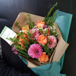 Bouquet of orange roses and pink dahlias wrapped in brown and teal paper