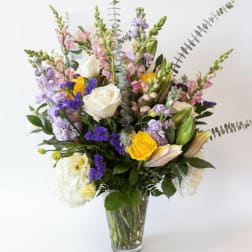 Mixed bouquet of roses, lilies, and purple flowers in a clear glass vase