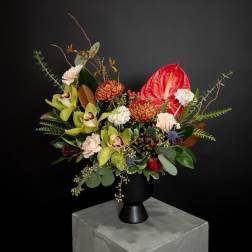 Mixed floral arrangement in a black vase with red anthurium and green orchids