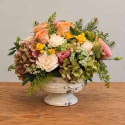 Mixed bouquet in a white pedestal vase with peach, pink, and yellow blooms