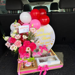 Pink and white floral gift arrangement with balloons, chocolates, and a birthday sign