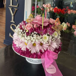 Pink floral arrangement with roses, daisies, and candles in a white pedestal bowl