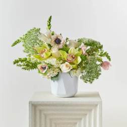 White vase with a pastel floral arrangement of orchids and roses