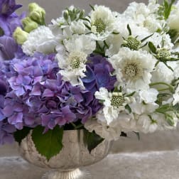 Purple and white floral arrangement in a decorative bowl vase
