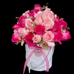Pink and white roses arranged in a white hat box with a pink ribbon