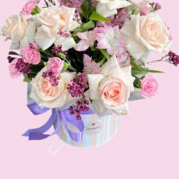 Pink and white roses arranged in a striped hat box with a purple ribbon
