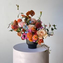 Mixed bouquet of orange, pink, and cream flowers in a black vase