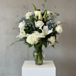 White roses and lilies arranged in a glass vase with blue accents