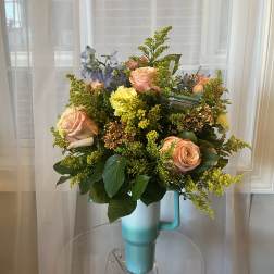 Bouquet of peach roses and yellow filler flowers in a turquoise mug vase