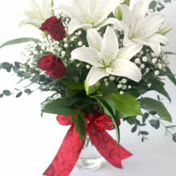 Bouquet of white lilies and red roses in a glass vase with a red ribbon