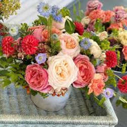 Colorful arrangement of pink and peach roses with red blooms and small blue flowers in a white pot