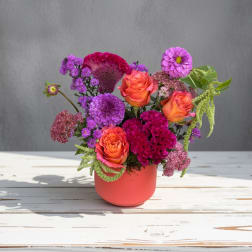 Colorful bouquet of roses and purple blooms in a coral vase